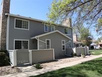Two-story townhome with gray siding, stone chimney, and a well-maintained front yard under a clear blue sky at 8418 Everett Way # C, Arvada, CO 80005