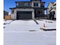 Charming two-story home featuring stone accents and a two-car garage with a snow covered driveway at 393 Grey Rock St, Brighton, CO 80601