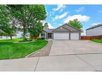 Charming home featuring a manicured lawn, mature trees, and a three-car garage with stone accents at 2205 Santa Fe Dr, Longmont, CO 80504