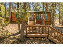 Exterior view of a wooden cabin surrounded by trees, featuring a deck and staircase, perfect mountain living at 5235 Cheyenne Rd, Indian Hills, CO 80454