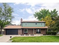 Charming two-story home with brick facade, lush lawn, mature trees, and attached two car garage at 6982 Estes Dr, Arvada, CO 80004