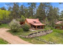 Charming log cabin with a red roof surrounded by lush greenery and mature trees at 245 N County Highway 67, Sedalia, CO 80135