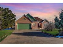 Beautiful brick home with an attached green garage and a well-manicured lawn at dusk at 4270 Defoe St, Strasburg, CO 80136
