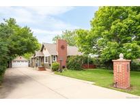 Charming exterior features a well-maintained lawn, a brick chimney, and a detached two car garage with a long driveway at 3317 Harlan St, Wheat Ridge, CO 80033