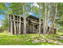 Charming brown two-story home with a green lawn and many aspen trees at 1927 Sunset Cir, Evergreen, CO 80439