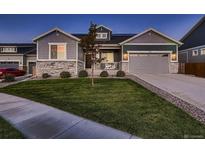 Charming two-story home with stone accents, a well-manicured lawn, and a driveway leading to a two-car garage at 11560 Kalispell St, Commerce City, CO 80022