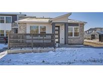 Charming modern home with stone accents, gray trim, and a small fenced yard with snow at 2507 W 69Th Pl, Denver, CO 80221