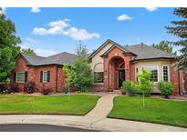 Charming red brick home features a manicured lawn, mature trees, and an inviting arched entryway, creating a welcoming curb appeal at 5926 S Elkhart Ct, Centennial, CO 80016