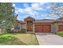 Charming stone home featuring a wooden garage door and a well manicured front yard at 1015 Nob Hill Rd, Evergreen, CO 80439