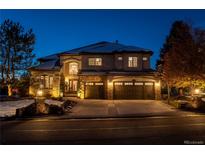 Stunning two-story stucco home with stone accents, a three-car garage, and inviting landscaping illuminated at twilight at 9445 Aspen Hill Cir, Lone Tree, CO 80124