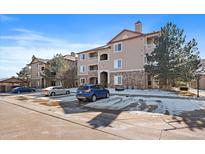 Three-story condo building with stone accents, covered balconies, and ample parking on a sunny day at 8445 S Holland Way # 207, Littleton, CO 80128