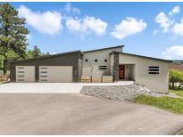 Modern home with a three-car garage, striking red door, and meticulously landscaped front yard with grey stucco and angular roofline at 3630 Mesa Verde Rd, Monument, CO 80132