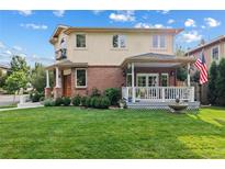 Charming two-story home featuring a brick facade, covered porch, well-manicured lawn, and lush landscaping at 2400 S Clayton St, Denver, CO 80210