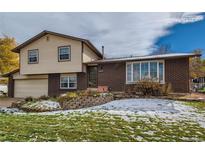 Split-level home features brick and vinyl siding, attached garage, and manicured front yard at 7218 W Frost Dr, Littleton, CO 80128