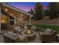 Relaxing outdoor patio with wicker furniture and a cozy stone fire pit under a wood-covered porch at 2832 Danbury Ave, Highlands Ranch, CO 80126