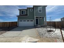 Two-story home with sage green siding, white trim, a two-car garage, and a newly planted tree in the front yard at 18348 E 93Rd Pl, Commerce City, CO 80022