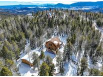 Aerial view of a stunning log home nestled in a snowy mountaintop forest at 11498 Pauls Ln, Conifer, CO 80433