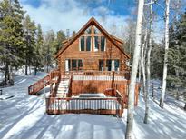 Charming log home featuring a spacious wooden deck and surrounded by mature trees in a serene, snow-covered setting at 11498 Pauls Ln, Conifer, CO 80433