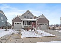 Charming two-story home featuring a covered porch, three-car garage and well-manicured front yard during winter at 848 Sandstone Cir, Erie, CO 80516