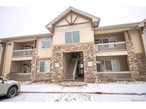 Exterior of the building with stone accents, multiple floors, and balconies covered in light snow at 10487 W Hampden Ave # 101, Lakewood, CO 80227