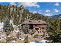 Beautiful exterior of a log home with mountain views, stone accents, and mature trees at 3999 Evans Ranch Rd, Evergreen, CO 80439