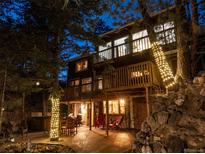 Stunning two-story home featuring a wooden deck, outdoor seating and trees wrapped in string lights at 9506 S Deer Creek Canyon Rd, Littleton, CO 80127