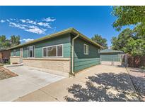 Charming home features a green exterior, brick accents, and a paved driveway leading to a detached garage at 5556 Vaughn St, Denver, CO 80239