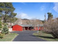 Red, ranch-style house with an attached garage and a paved driveway in a wooded area at 96 Greeley Blvd, Palmer Lake, CO 80133