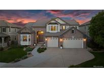 Elegant brick home with a three-car garage, landscaped front yard, and warm exterior lighting at 6095 S Oswego St, Greenwood Village, CO 80111