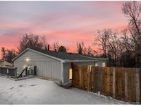 This home features gray siding, wood fence, and snow covered yard at dusk at 3398 Wadsworth Blvd, Wheat Ridge, CO 80033