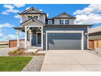 Two-story home with blue siding, a gray garage door, front porch, and professionally landscaped front yard at 2237 Garden Ave, Brighton, CO 80601