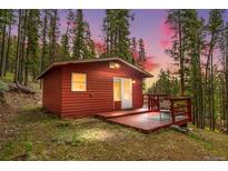 Charming red cabin nestled in a forest setting with a cozy deck, perfect for enjoying nature at 154 Apache Rd, Evergreen, CO 80439