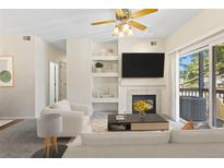 Bright living room with a fireplace, built-in shelves, ceiling fan, and sliding glass doors to a balcony at 10784 W 63Rd Pl # 205, Arvada, CO 80004