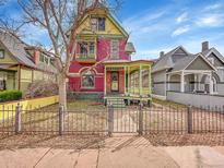 Charming red Victorian home with a landscaped yard, black iron fence and inviting front porch with decorative trim at 3424 N Marion St, Denver, CO 80205