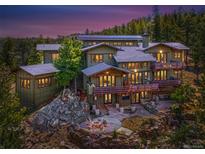 Expansive home featuring multi-tiered decks and stone patio with fire pit, surrounded by lush trees and rocky landscape at 3395 Timbergate Trl, Evergreen, CO 80439