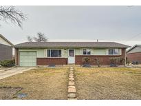 Charming ranch-style home with a brick facade, green paint, and a well-manicured front yard with rock path at 14937 E Security Way, Aurora, CO 80011