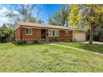 Inviting single-story brick home with a lush green lawn, mature tree, and attached garage at 8660 De Soto St, Denver, CO 80229