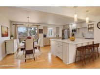 Bright, open kitchen with island, breakfast bar, light wood floors, and adjacent dining area at 3785 S Benton Way, Denver, CO 80235