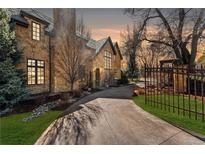 Stone home featuring a long driveway, manicured lawn, and mature trees under a colorful sunset at 4160 S Humboldt St, Cherry Hills Village, CO 80113