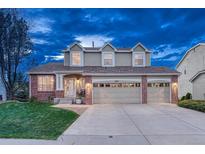 Inviting two-story home featuring a three-car garage, brick accents and well-manicured lawn at twilight at 6973 Daventry Pl, Castle Pines, CO 80108