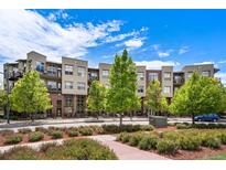 Modern condo building with a mix of brick and siding, balconies, and landscaped greenery under a bright blue sky at 7700 E 29Th Ave # 404, Denver, CO 80238