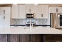 A modern kitchen with stainless appliances, white cabinetry, and a spacious quartz island at 7041 E Girard Ave, Denver, CO 80224