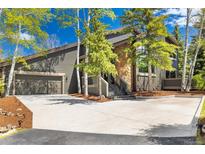 Inviting exterior featuring stone accents, mature trees, a spacious driveway, and an attached two car garage at 2140 Torrey Pine Dr, Evergreen, CO 80439