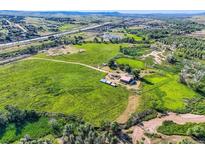 Expansive aerial view of a farm with large grassy fields, outbuildings, and a stream winding through the landscape at 11475 Us Highway 85, Littleton, CO 80125