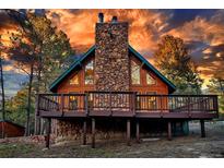 Stunning exterior view of a wood cabin featuring a stone chimney and wraparound deck in a wooded setting at 36920 Forest Trl, Elizabeth, CO 80107