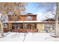 Charming two-story home featuring a stone facade, inviting front porch, and snow-covered yard at 9770 Quitman Way, Westminster, CO 80031