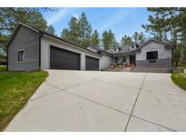 Beautiful gray home with large driveway and a three car garage with trees in the background at 929 Tenderfoot Dr, Larkspur, CO 80118
