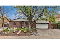 Charming brick home featuring a two-car garage, landscaped front yard, mature tree, and concrete driveway at 6235 W Floyd Ave, Denver, CO 80227