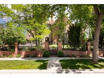 Charming brick home with manicured front lawn, mature trees, and secure iron gate and fence at 100 N Gaylord St, Denver, CO 80206