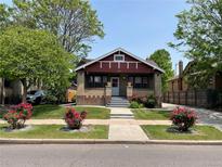 Charming brick home featuring a cozy front porch and a well-manicured lawn with vibrant rose bushes at 1418 Perry St, Denver, CO 80204